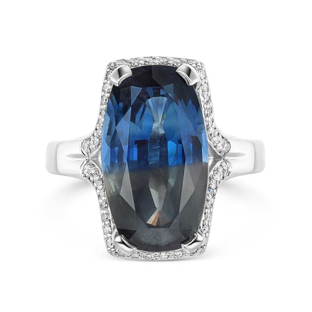 Parti sapphire in blue and grey tones, surrounded by a halo of round brilliant cur diamonds set in a platinum band on a white background