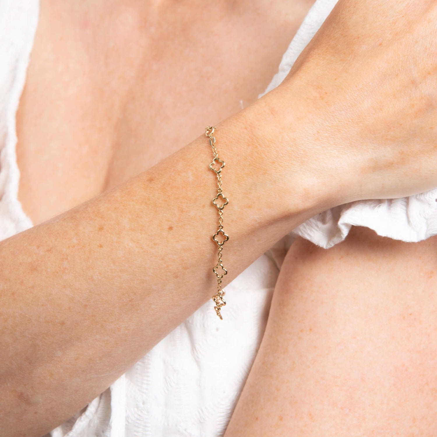 Gold clover shaped link bracelet on a person's wrist with a white background