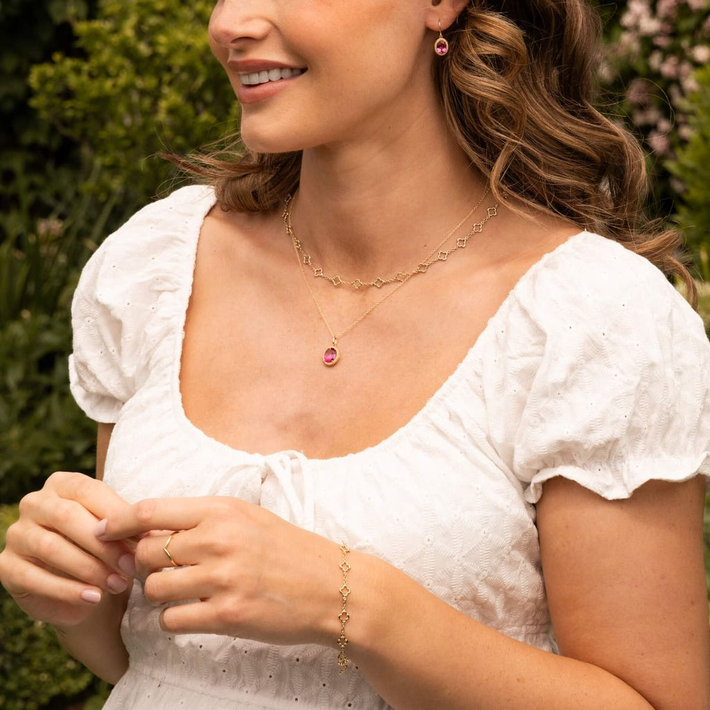 Woman wearing a white blouse with visible clover shaped link jewellery outdoors
