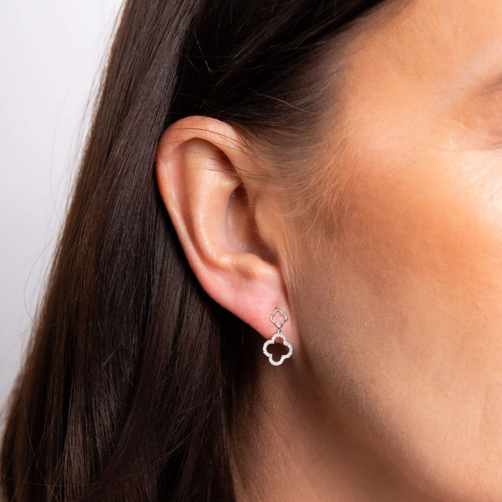 Close-up of an ear wearing a clover-shaped earring with a neutral background