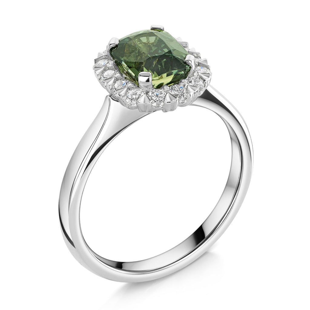 A silver ring featuring a cushion cut green sapphire surrounded by a halo of small white diamonds, set on a polished platinum band against a white background.