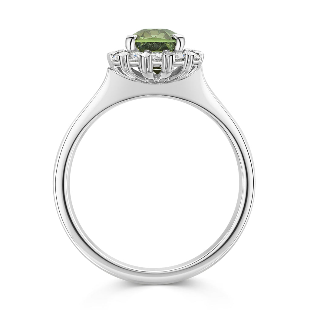A silver ring featuring a cushion cut green sapphire surrounded by a halo of small white diamonds, set on a polished platinum band against a white background - side view
