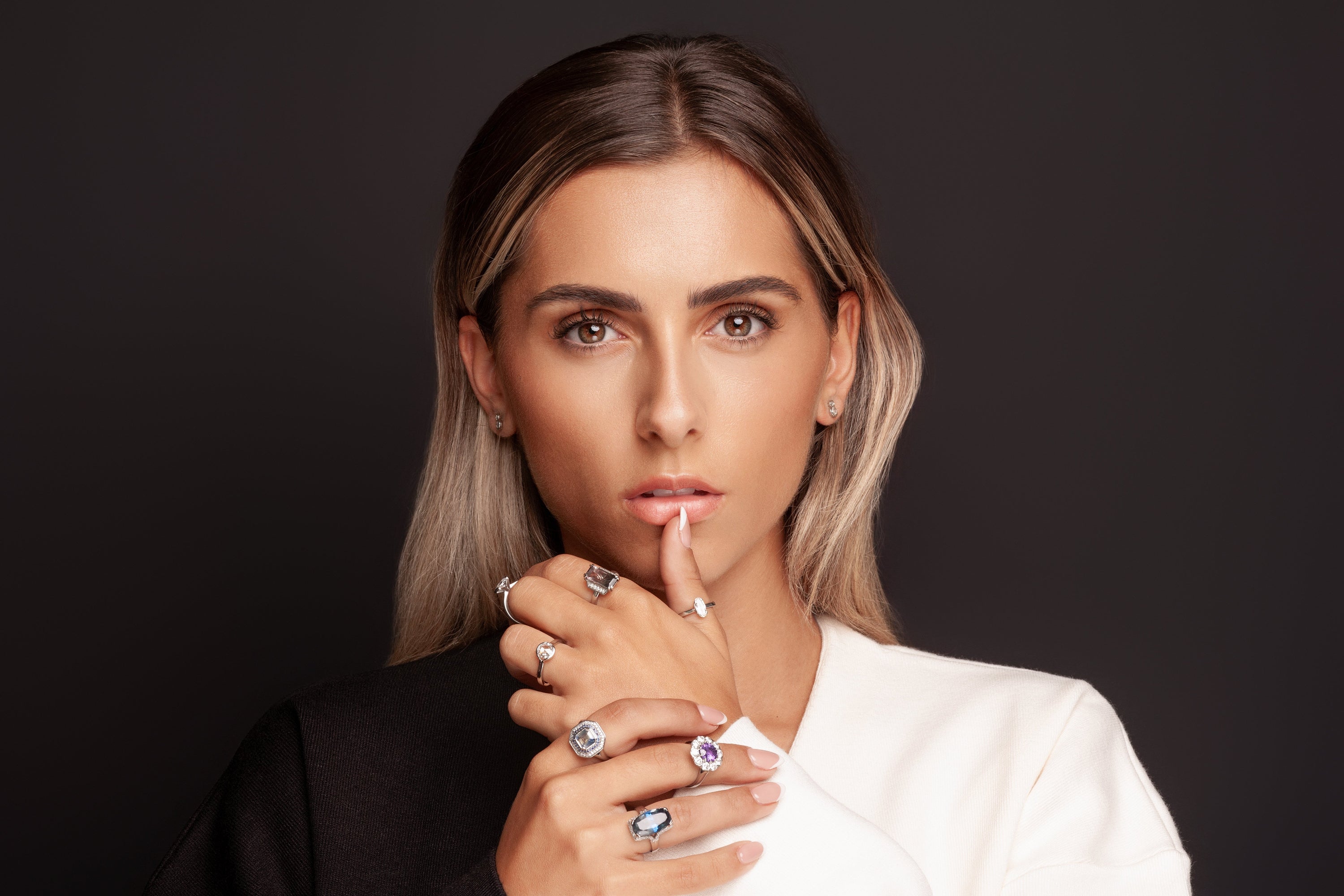 Woman wearing multiple rings on her fingers against a dark background