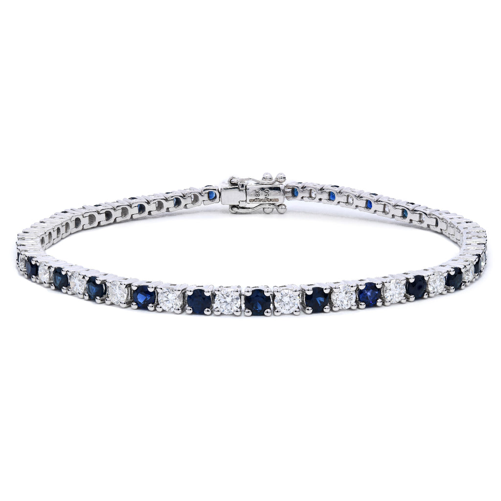 Sapphire and diamond tennis bracelet with alternating diamonds and blue sapphires in claw setting on a white background.