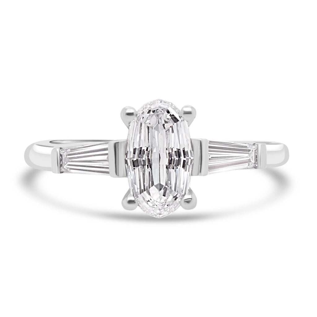 step cut oval diamond trilogy ring with tapered baguettes on white background
