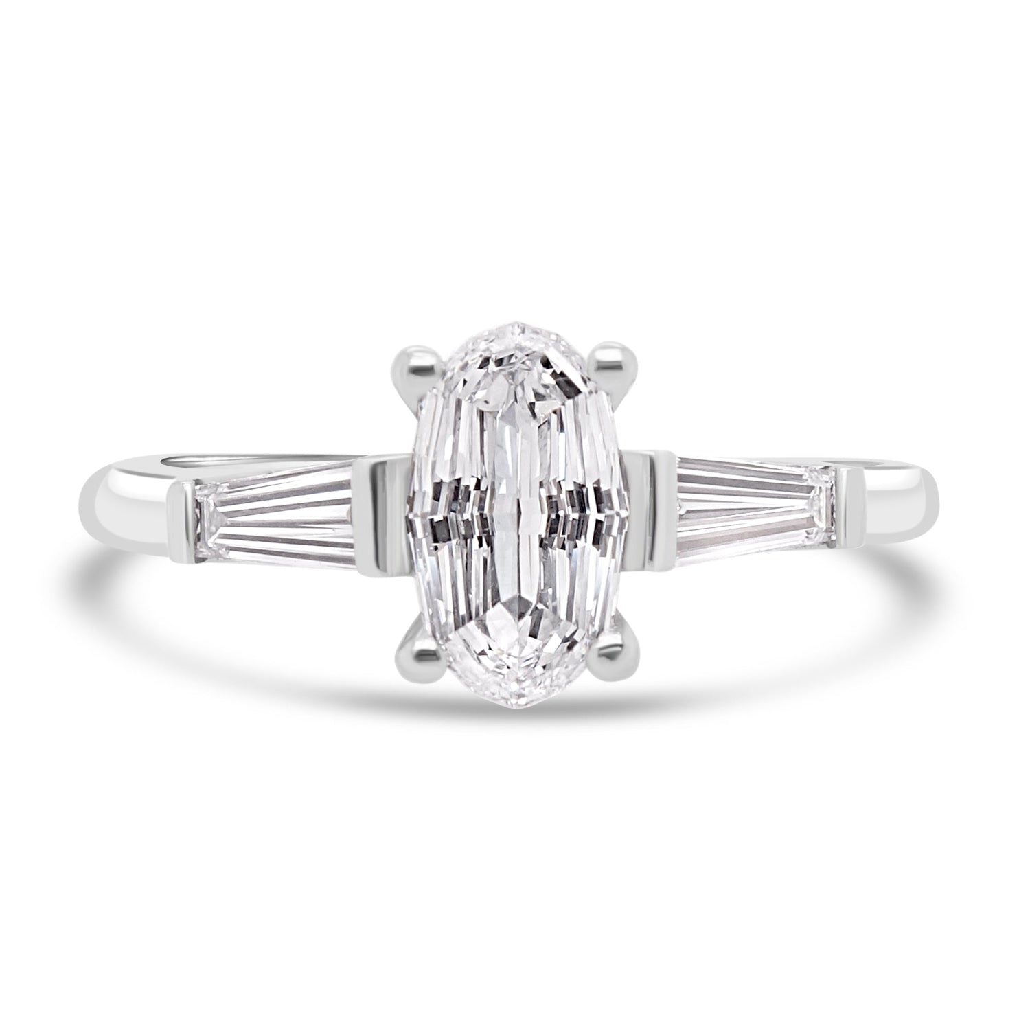 step cut oval diamond trilogy ring with tapered baguettes on white background