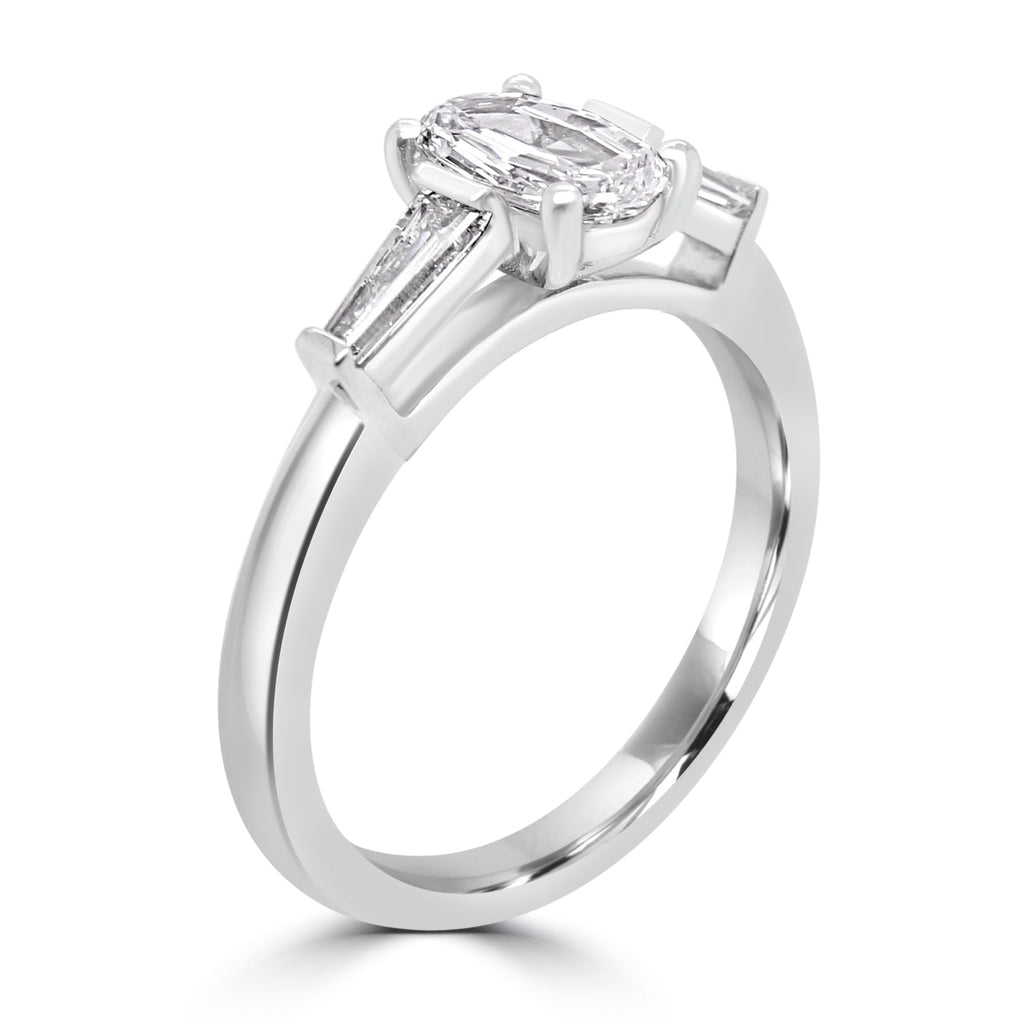 step cut oval diamond trilogy ring with tapered baguettes - angled view on white background